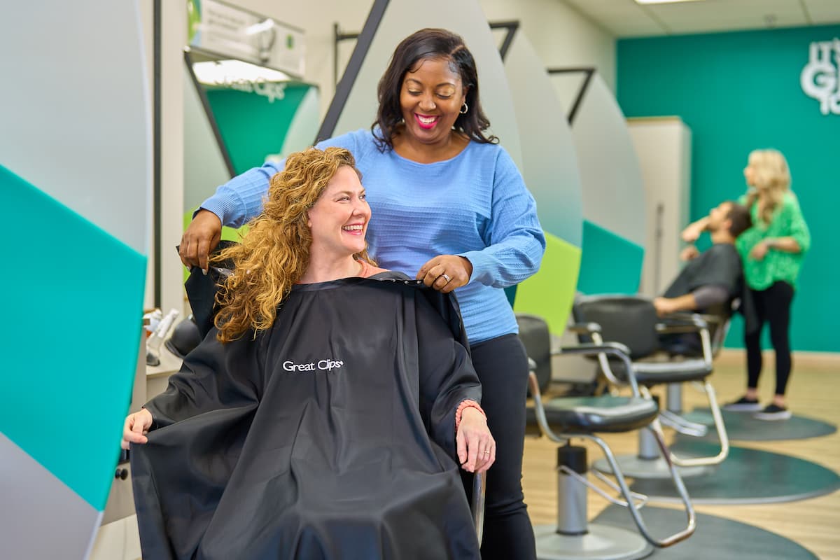 Great Clips stylist and customer smiling at each other as the stylist prepares to cut the customer's long curly hair